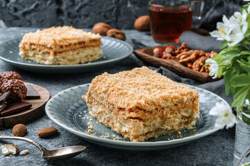 Slices of Napoleon cake with cream and nuts on plate over grey background. Sweets, dessert and pastry, millefeuille cake, top view, close up