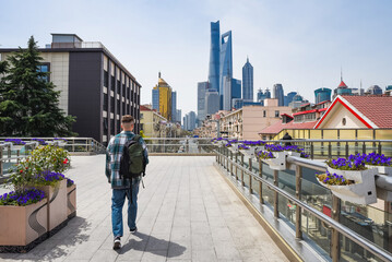 Fototapeta premium Wide view of a tourist crossing a bridge in Pudong, Shanghai, with blooming flowers and the skyline featuring Shanghai Tower and SWFC.