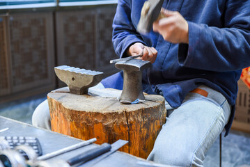 Craftsman in Shanghai market shapes metal jewelry by hand using a hammer and anvil. Traditional tools and skills used to make rings or bracelets