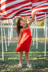 Smiling girl in red dress looking at American flag on Memorial Day, USA