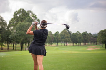 Professional female golfer lush green golf course, mid-swing after hitting a shot through after driving the ball down the fairway trees and distant sand bunkers, typical of a competitive setting.  