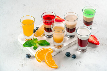 Various alcoholic drinks in glasses on a white table, mixed shots of berries and oranges