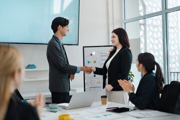 Diverse business professionals celebrating a successful partnership with a handshake in a modern office.