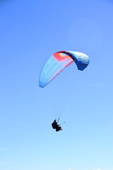 Paraglider flying over a mountain range. Outdoor adventure, scenic backdrop under a vivid blue sky