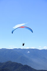 Paraglider flying over a mountain range. Outdoor adventure, scenic backdrop under a vivid blue sky