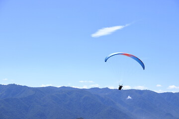 Paraglider flying over a mountain range. Outdoor adventure, scenic backdrop under a vivid blue sky