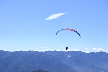 Paraglider flying over a mountain range. Outdoor adventure, scenic backdrop under a vivid blue sky
