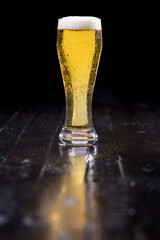 Close up of a golden lager on a wooden table with a slight reflection over a dark background.