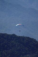 Paraglider flying over a lush forest landscape enveloped by mist. Outdoor adventure, scenic...