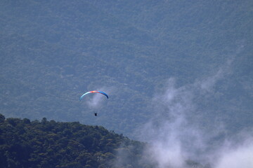 Paraglider flying over a lush forest landscape enveloped by mist. Outdoor adventure, scenic...