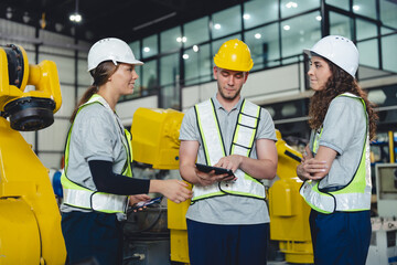 Industrial engineers collaborate in a high-tech factory environment, inspecting robotic machinery...