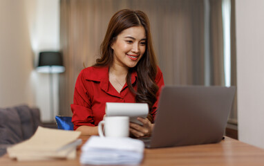 Happy asian woman using laptop while working remotely from home in living room
