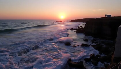 Dramatic coastline sunset with ocean waves and silhouette figure atop a cliff