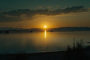 Obraz premium Golden sunset over calm lake with wind turbines. Silhouette of a pier extends into the water