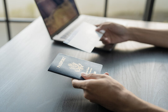 Hand Man Online booking and buying plane tickets using laptop phone and credit card Planning trip travel vacation with passport and ticket.
