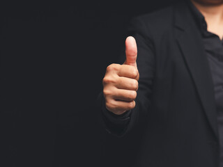 Businessman showing thumbs up gesture against black background, symbol of approval or success.