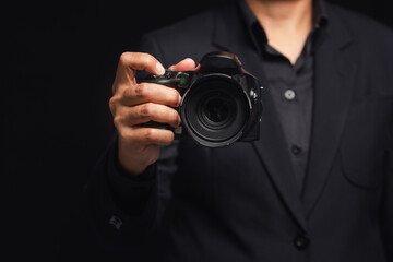 Photographer in black suit holding DSLR camera against dark background, concept of portrait work.