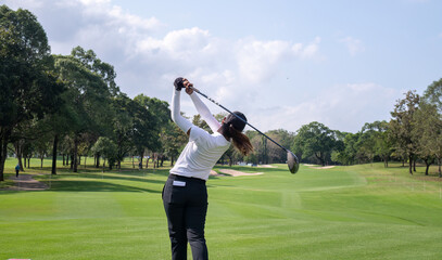 Professional female golfer lush green golf course, mid-swing after hitting a shot through after driving the ball down the fairway trees and distant sand bunkers, typical of a competitive setting.  