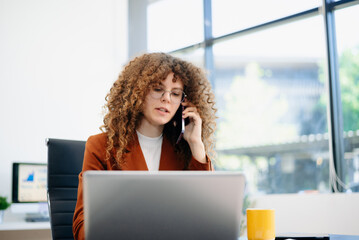 an in rust suit multitasking with phone and documents at laptop desk in bright office. Concept of...