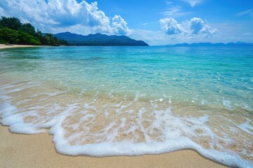 Waves gently washing ashore on a tropical beach with mountains in distance