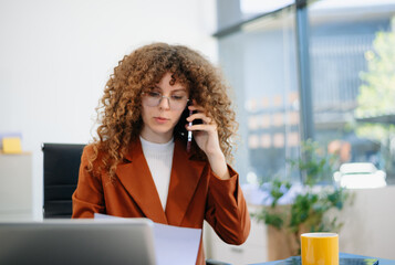 an in rust suit multitasking with phone and documents at laptop desk in bright office. Concept of...