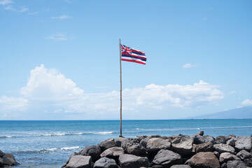Hawaiian Flag Flying on a Rocky Shore by the Ocean