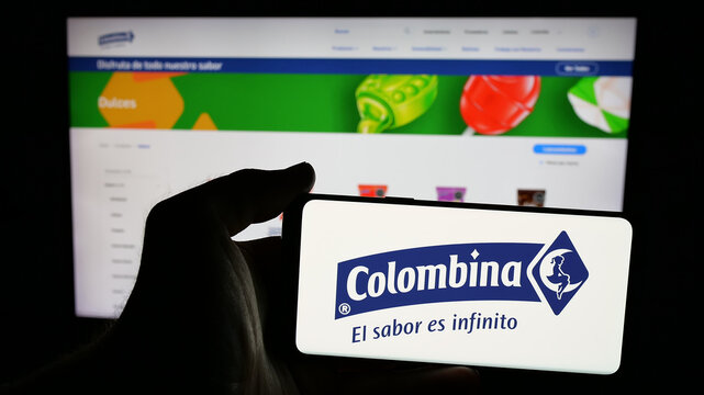 Stuttgart, Germany - 05-04-2025: Person holding mobile phone with logo of food processing company Colombina S.A. on screen in front of web page. Focus on phone display.