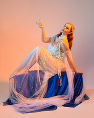 Fantasy studio portrait of a red-haired mermaid faery model wearing a white pearl gown, fairytale...