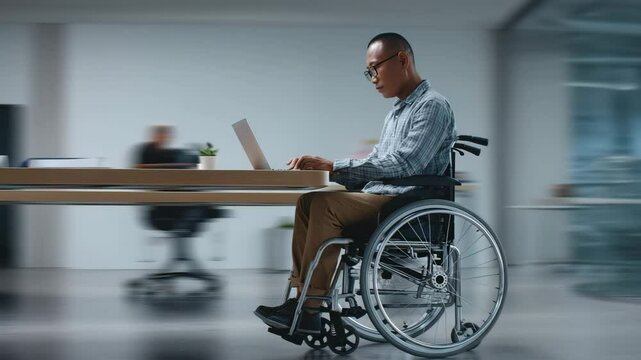 Mature man in a wheelchair working professionally on a laptop in a modern corporate office, representing inclusion and productivity.

