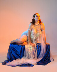 Fantasy studio portrait of a red-haired mermaid faery model wearing a white pearl gown, fairytale...