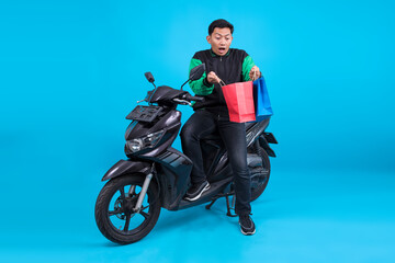 Shocked Asian Driver Man Sitting on Motorbike and Open Shopping Bags Over Blue Background