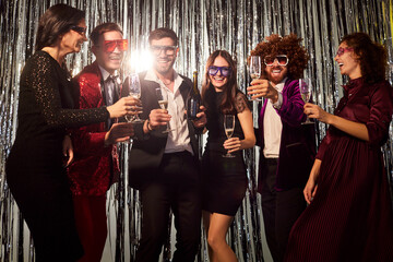 Group of cheerful friends dancing while holding champagne glasses at an evening party in a...