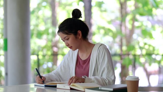 Focused Study: A young woman engrossed in her studies at a table, pen poised over paper. The image conveys a sense of concentration and studiousness.