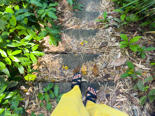 Top view of woman wear sandals and yellow pants walking on steps in the green forest.
