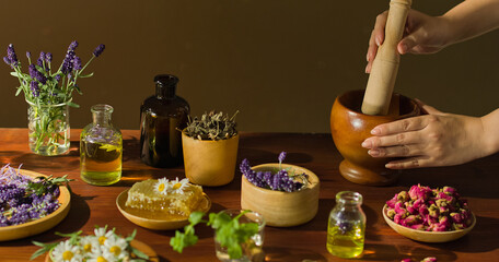 A traditional Chinese medicine practitioner is using a pestle to crush herbs in a wooden mortar. Medicinal plants are displayed on a wooden table, which are natural ingredients for making medicine.