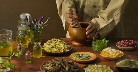 Herbalist using a pestle to crush herbs inside a mortar. There are various glass jars containing...