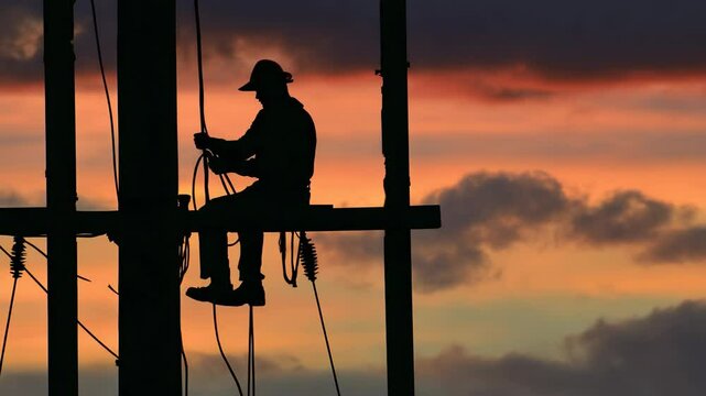 Silhouette of worker on utility pole at sunset.