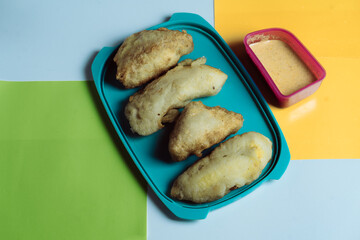  A vibrant flat lay image showcasing five pieces of deep-fried snacks arranged on a bright turquoise tray, accompanied by a small container of creamy dipping .