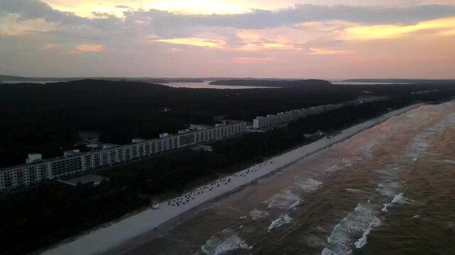 Golden sunset over the historic Prora complex in R&uuml;gen, with waves gently rolling onto the sandy shoreline.