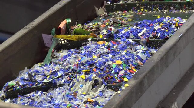Waste Sorting at a Recycling Plant. Plastic recycling plant.  Recycled of plastic bottle cap factory, manufacturing process of polyester fibre. Conveyor with shredded plastic from PET bottles.
