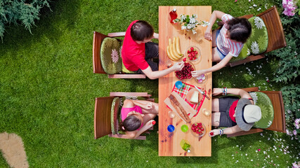 Family and friends eating together outdoors on summer garden party in park. Aerial view of table with food and drinks on grass from above. Leisure, holidays and picnic concept