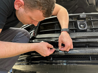 A car wrapping specialist applies a polyurethane film to the car. Selective focus. PPF protective film against chips and scratches. Car wrapping, detailing, tuning and styling. Detailer smoothes PPF. 