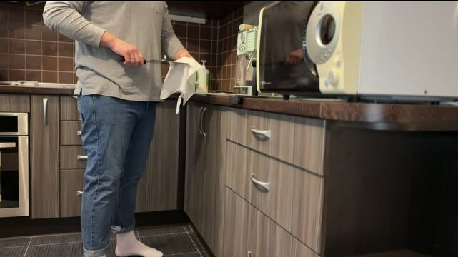 A man in a kitchen pulls out a meat cleaver and carefully wipes it with a cloth, without any violence or blood.
