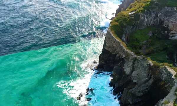 Aerial footage of turquoise ocean waters washing rugged, rocky shoreline