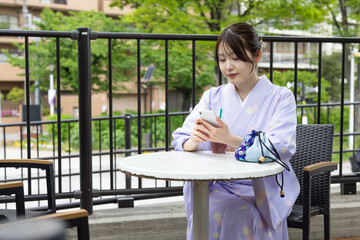 カフェのテラス席でスマートフォンを操作する着物を着た若い日本人女性