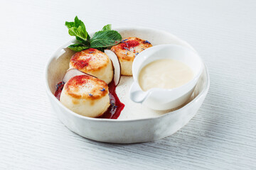 Dessert on white plate with mint leaves. Elegant breakfast with cottage cheese pancakes, berry sauce, and cream