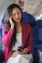 Businesswoman suffering headache holding smartphone on airplane