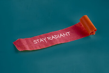 A colorful ribbon featuring the encouraging phrase stay radiant is rolled up, showcasing an...