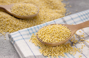 Millet grains in wooden spoon on a gray background