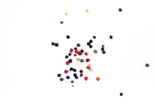 Close-up of peppercorns - red, green, black and white, scattered chaotically on a white background, aromatic spice, macro photography.